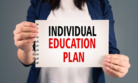 A woman holding a notepad with "individual education plan" written on it, on a gray background, stock photoの写真素材