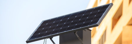 Public urban light with a solar panel working on a blue sky with clouds.