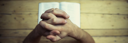 Praying hands with bible on the wooden desk background.