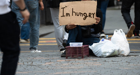 A beggar on a city street holding a cardboard with "I'm hungry" written on itの写真素材