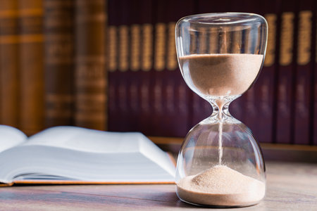 Hourglass and opened book on library table