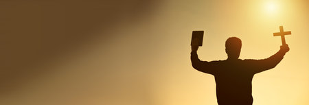 hands holding wooden cross and bible on sunrise backgroundの写真素材