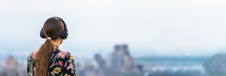 A young girl listens to music in headphones on the background of the cityの写真素材