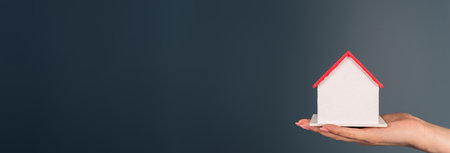 Woman holding a model of a house in her hand on a gray backgroundの写真素材