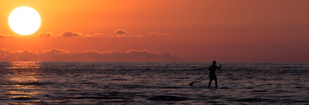 People surfing with a paddle in the sea at sunset