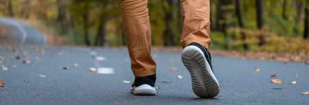 Autumn Stroll: Close-Up of Young Man's Legs Walking on the Roadの写真素材