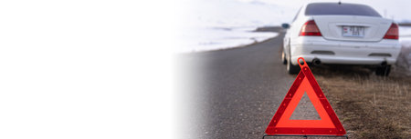 White car on winter road, warning red triangle sign in foregroundの写真素材