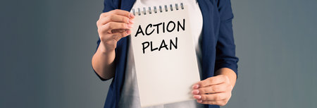 A woman holding a notepad with "action plan" written on it, on a gray background, stock photoの写真素材