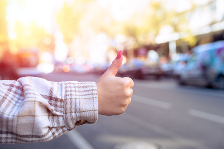 A woman with her thumb up while hitchhiking on the street