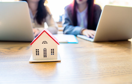 In a real estate office selling houses, women work on laptops, a small house on the tableの写真素材