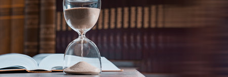Hourglass and opened book on library table