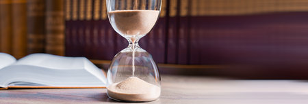 Hourglass and opened book on library table