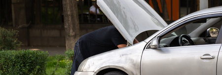 A man is trying to repair his broken car on the street, the hood is openの写真素材