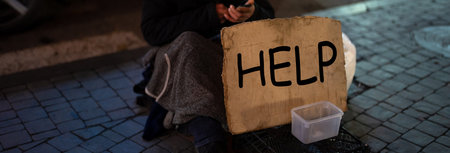 A homeless man is outside in the winter, with a cardboard sign in front of him that says "help"の写真素材