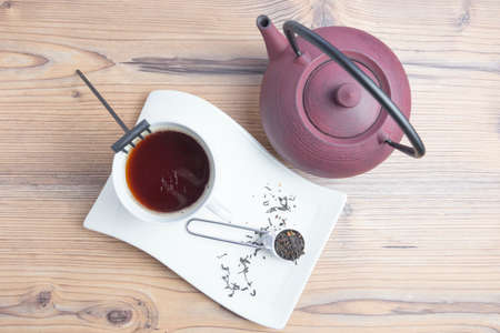 White porcelain tea cup, cast iron teapot with wooden spoon and black tea. Top view. Tea making...