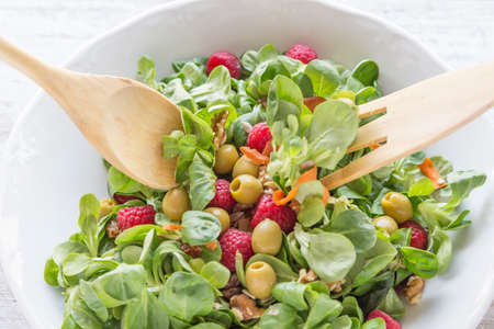 Salad of canons, raspberries, raisins, olives, nuts, carrots and pips. Wooden spoon and fork.の写真素材