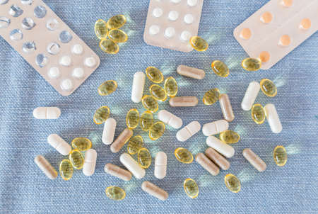 Tablets and capsules are scattered on the table. Blue background. Assorted pharmaceutical medicine...
