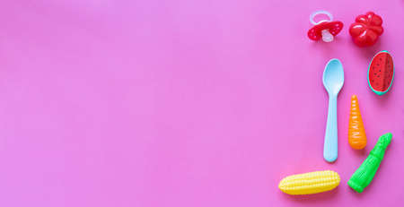 Infant baby food. With baby accessories and toys pink background. Copy space. Corn, carrot, tomato,...