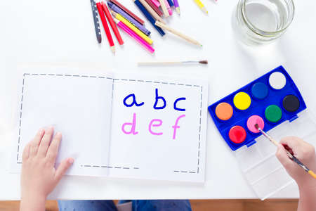 Charming little girl painting using watercolors sitting on a chair. Top view. Girl learning alphabet.の写真素材