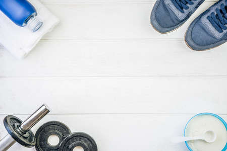 Fitness equipment. Sneakers, water, dumbbells and proteins on white wooden background. Top view, copy space.の写真素材