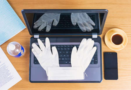 The top view of the Workspace during the Covid19 Coronavirus is spreading with a laptop computer, nose mask, glasses, a cup and hand sanitizer.の写真素材