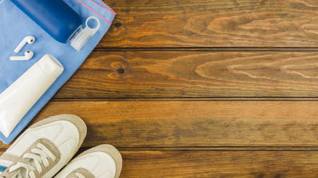 Fitness equipment top view with copy space. Water bottle, sport shoes, headphones and sun cream on wooden background.の写真素材