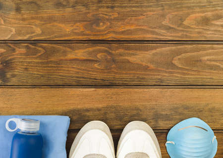 Fitness equipment top view with copy space. Water bottle, sport shoes and protective mask on wooden background.の写真素材