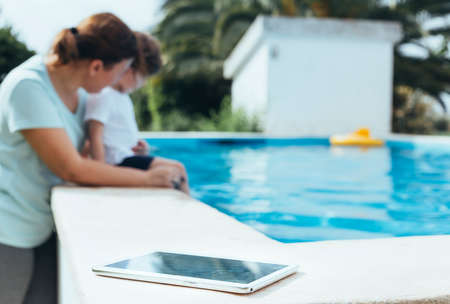 Digital Tablet photo in the foreground with mother and son playing in the pool in the background....
