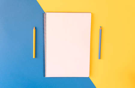 Empty notebook and pencils on yellow and blue background, Top view. Copy space.