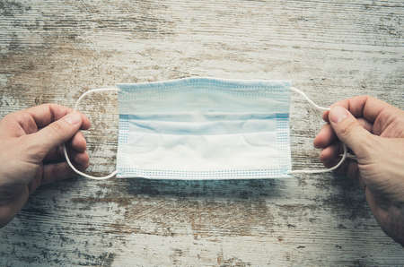 Man hands holding facial medical mask, wooden background, close up, copy space, banner. Flu epidemic, allergy season. Coronavirus, covid-19 protection.の写真素材