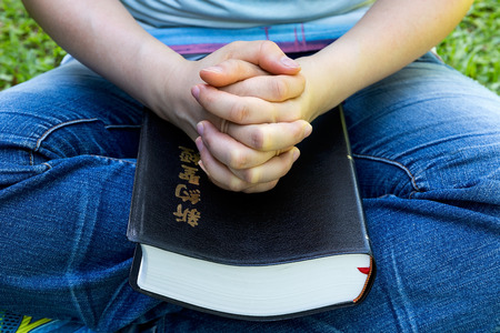 Woman hands praying with a Chinese New Testament holy bible in his legs Outdoorsの写真素材