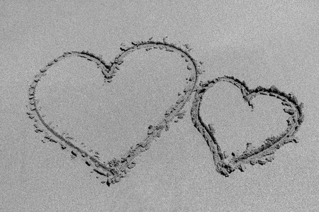 Two of hearts shapes drawn on a sandy sea beach (black and white)の写真素材