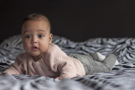 Portrait of a 3 months old baby girl lying on belly on parents bed looking in the camera