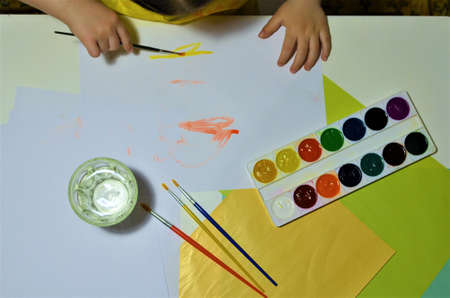 Children's hands when drawing. Desktop. Hobby. Table, colored, white and painted paper. Preschool...