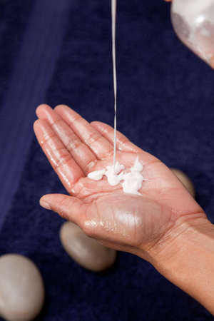 Massage oil and cream dripped into hand, with a blue towel background.の写真素材