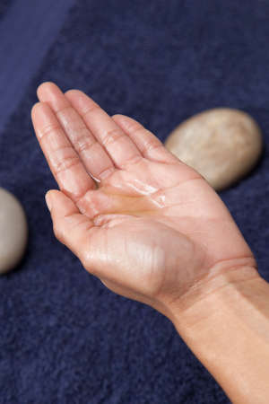 Massage oil and cream dripped into hand, with a blue towel background.の写真素材