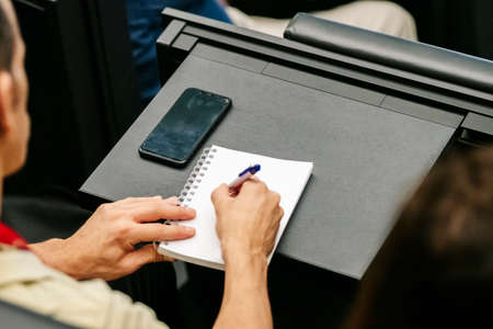 Detail of a woman's hands writing in a notebook at a congress