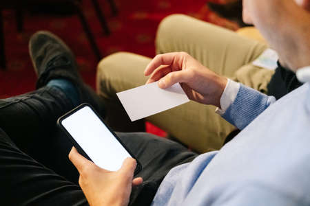 A man in a meeting looks at a business card and uses his mobile phoneの写真素材