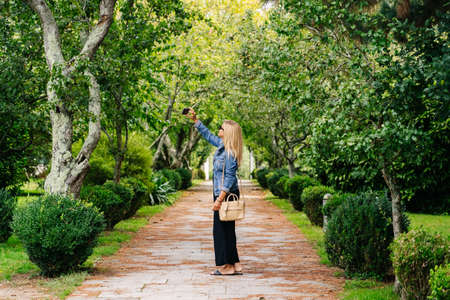 A beautiful caucasian blonde woman uses the phone to make a selfie in a parkの写真素材