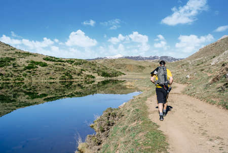 A man makes trekking walking along a road with a lake next to it and mountains