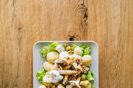 Plate with a delicious salad of lettuce, potato, cheese and nuts on a wooden table. Healthy life conceptの写真素材