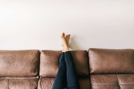 a woman's legs raised up high on the brown sofa at homeの写真素材