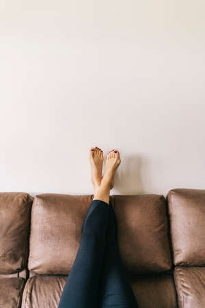 a woman's legs raised up high on the brown sofa at homeの写真素材