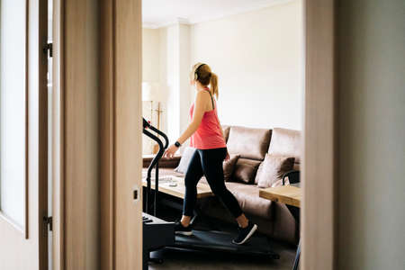 Beautiful caucasian blonde woman exercises on a treadmill in her living roomの写真素材