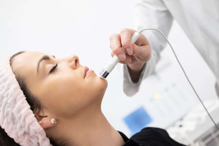 A beautiful girl doing facial care analyzing the skin of the face with a health and beauty device in a cosmetic clinicの写真素材