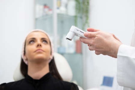 A beautiful girl doing facial care analyzing the skin of the face with a health and beauty device in...