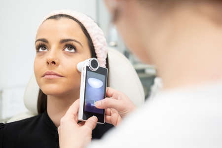 A beautiful girl doing facial care analyzing the skin of the face with a health and beauty device in a cosmetic clinicの写真素材