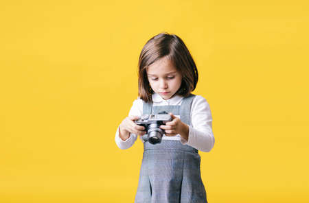 Portrait of a girl using a photo camera on yellow background. Pic with copy space.の写真素材