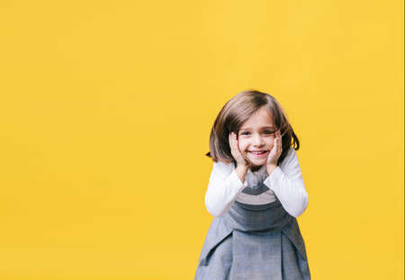A happy little girl laughing surprised with her hands on her face in amazement on yellow background. Photo with copy space.の写真素材