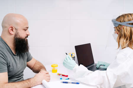 A female doctor does a swab test on a patient man in the hospital. She is wearing protective...